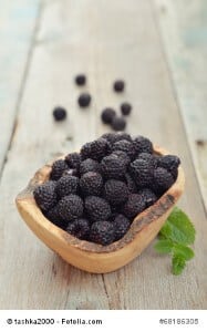 Blackberry in wooden bowl on wood background closeup