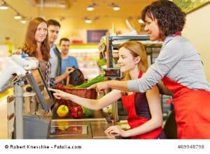 Ältere Verkäufer hilft einer neuen Kassiererin an der Kasse im Supermarkt